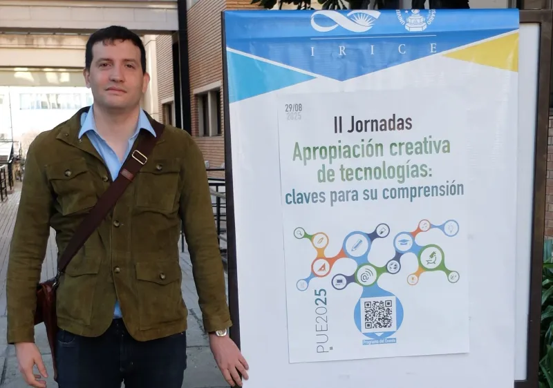 Ramiro Della Mea Guerrero de pie junto al cartel de las II Jornadas «Apropiación creativa de tecnologías: claves para su comprensión» del IRICE